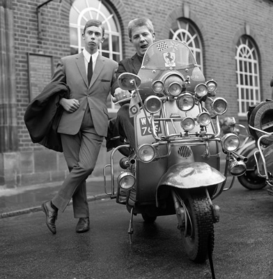 Modsi — dwóch mężczyzn w garniturach obok skutera Lambretta obwieszonego lusterkami i reflektorami