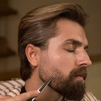 Barber przycina nożyczkami gęstą brodę mężczyzny — jak przycinać i pielęgnować zarost
